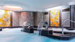 A spa area with a hot tub, two water jets, and a decorative wall with a floral pattern.