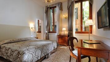 A hotel room with a bed, a desk, a chair, a television, and two windows with curtains.
