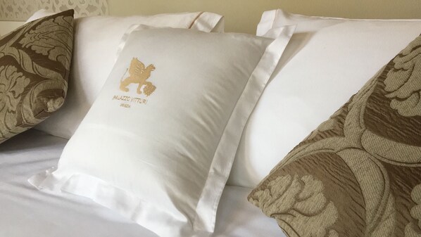 A bed with white pillows and a decorative pillow with a gold emblem and text.