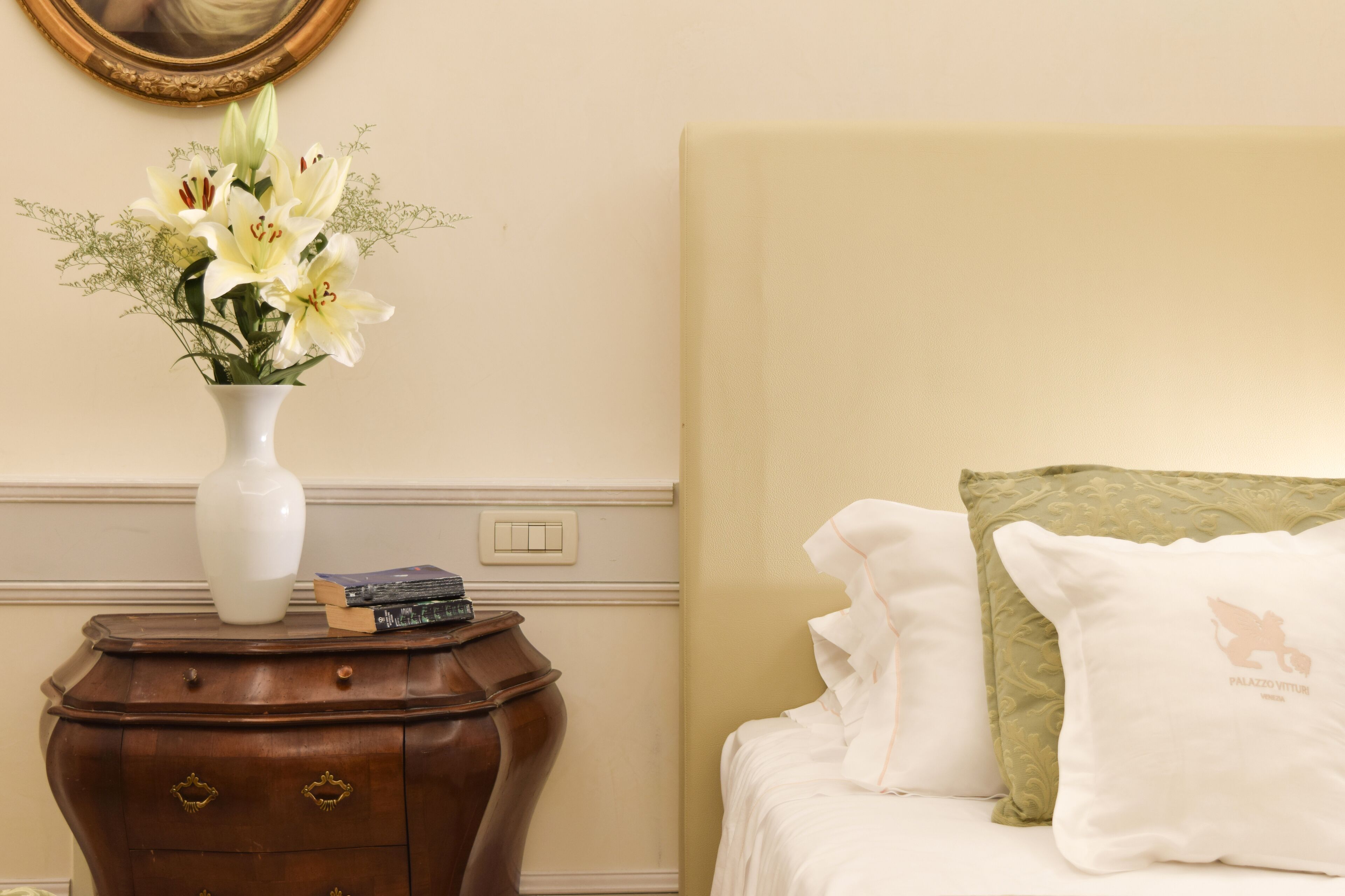 Une chambre à coucher avec un lit, des oreillers, une table de chevet ornée d’un vase de fleurs et un livre.