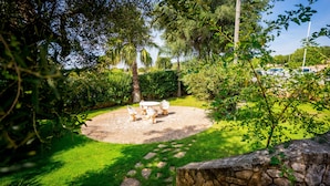 A circular outdoor seating area with stone steps leading up to it, surrounded by lush greenery and a stone wall. - Città Bianca Country Resort (Ostuni)