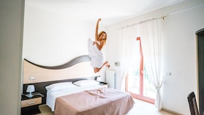 A bedroom with a bed, bedside table, lamp, and a window with curtains. - Città Bianca Country Resort (Ostuni)