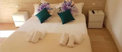 A neatly made bed with two pillows, a bedside table with a lamp, and a nightstand with a phone.