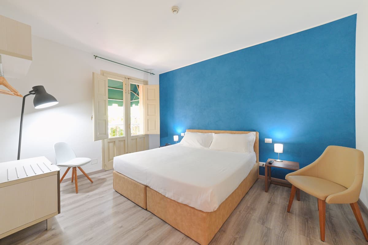 A bedroom with a bed, bedside tables, a chair, a desk, and a lamp.