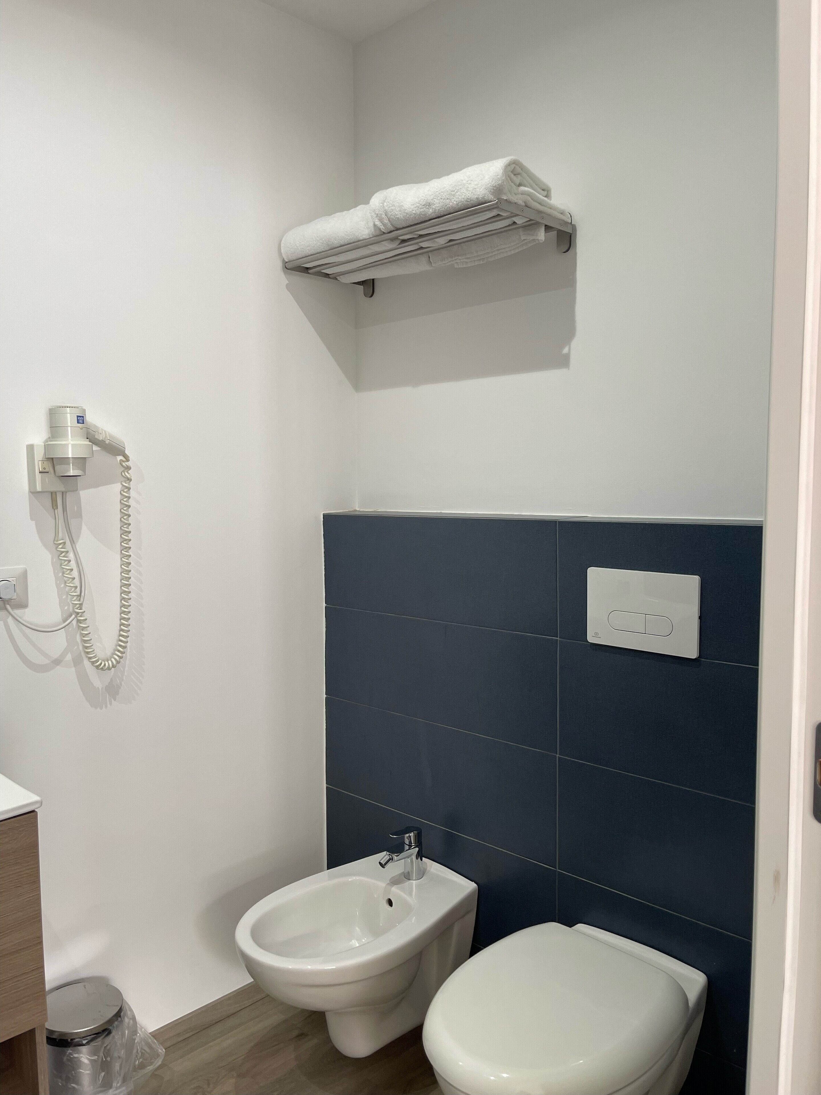 Een kleine badkamer met een bidet, toilet, handdoekhouder en een stopcontact aan de muur.