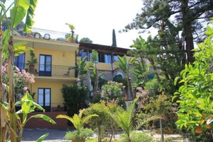 Un edificio amarillo con balcones y un jardín con diversas plantas.