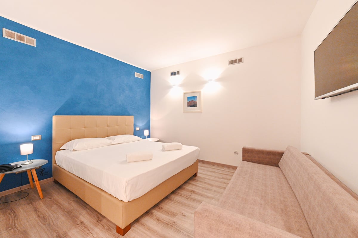 A bedroom with a bed, bedside table, lamp, and a wall-mounted TV.