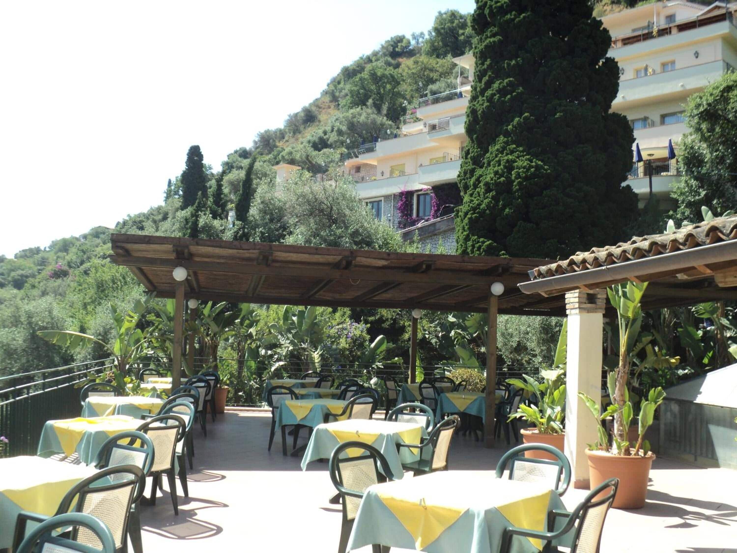 An outdoor patio with tables and chairs, surrounded by greenery and overlooking a hillside.