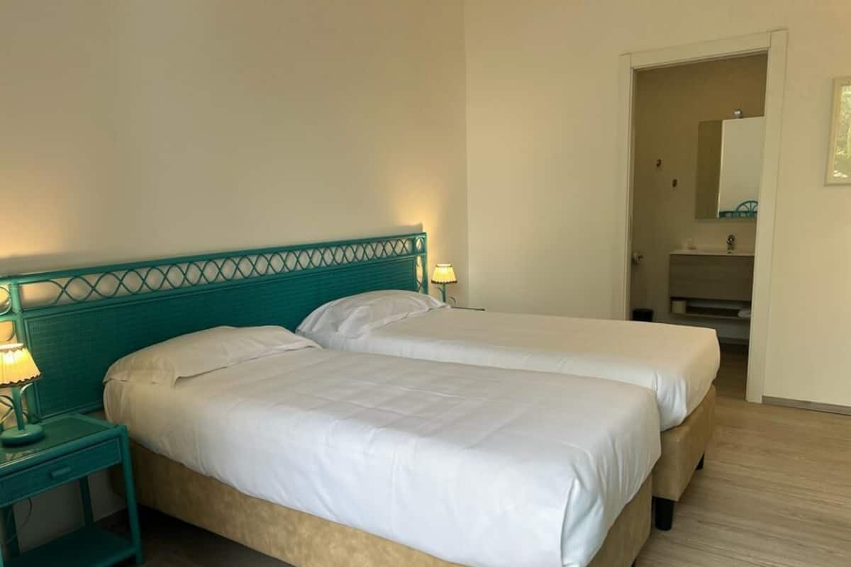 A double bed with a teal headboard, two bedside tables with lamps, and a wooden floor.
