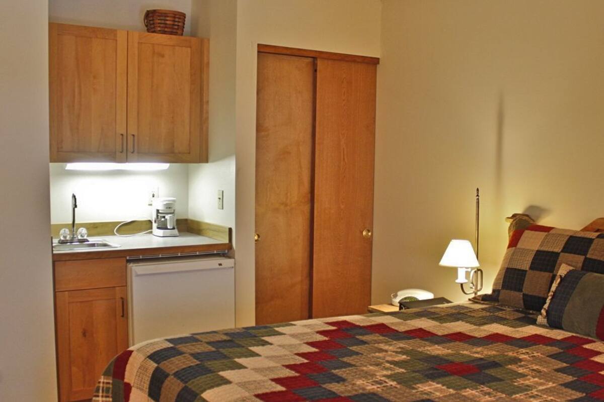 A compact room with a bed, a small kitchenette, and a wooden wardrobe.