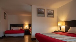 A hotel room with two beds, each with a red bedspread, a nightstand with a lamp, and a wall-mounted picture.