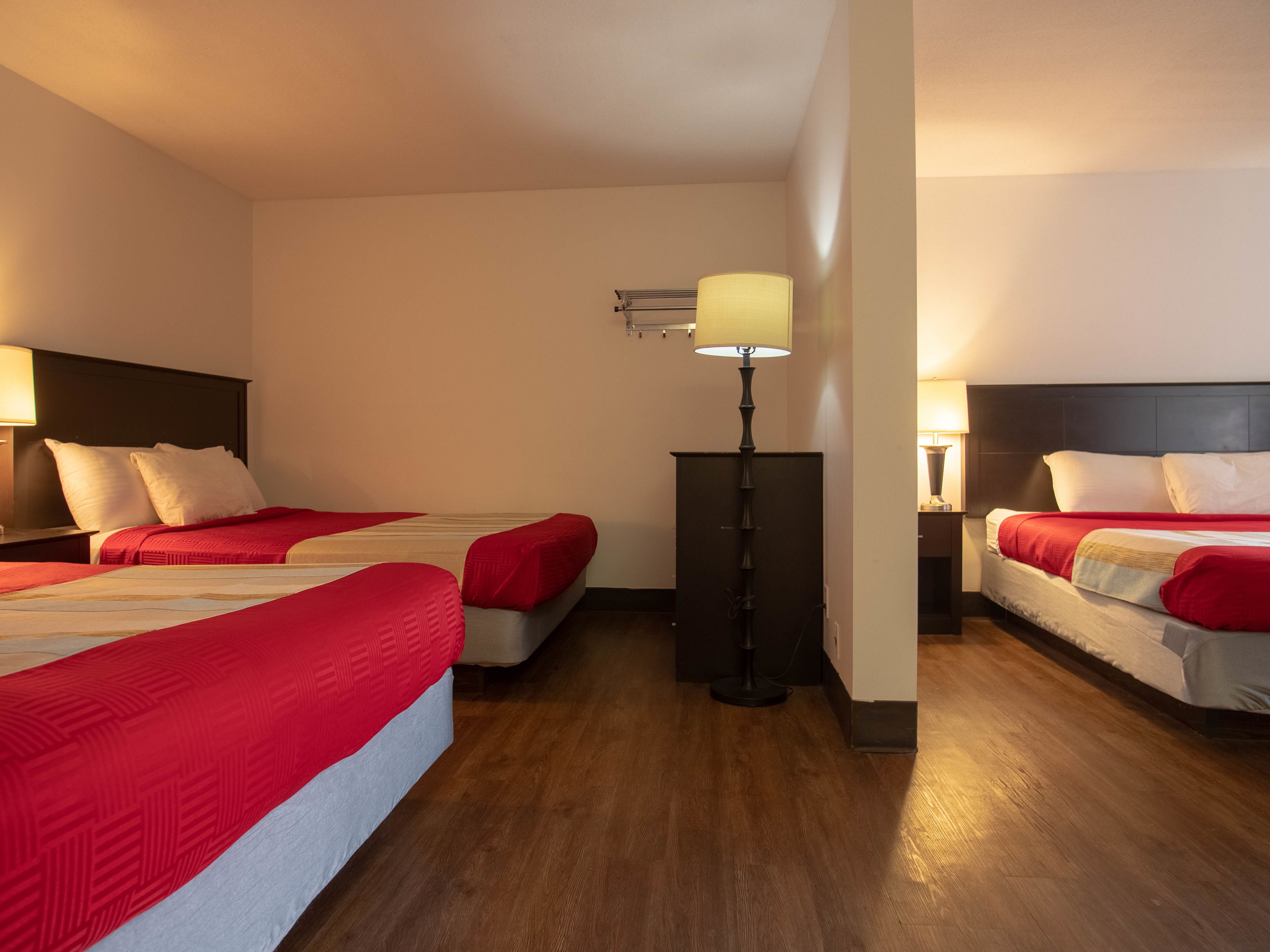 A hotel room with two beds, a standing lamp, and a nightstand with a lamp.