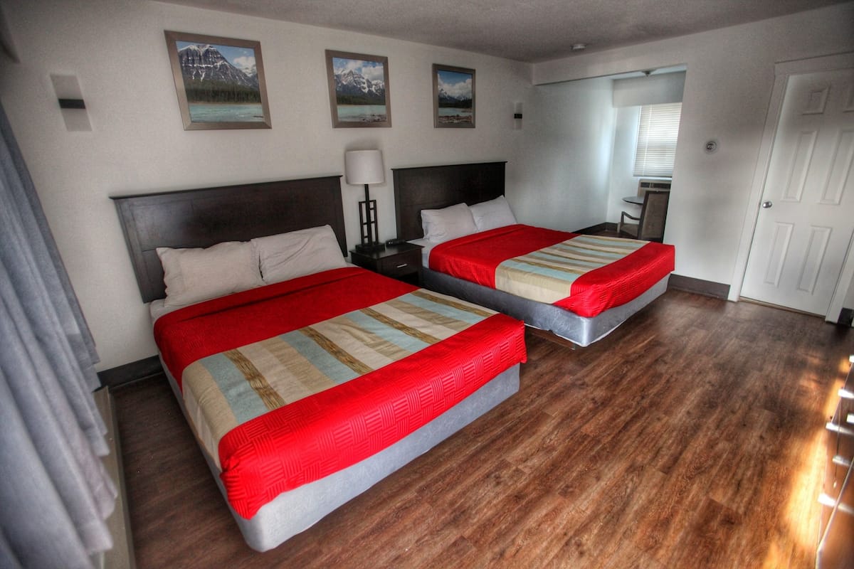 Ein Hotelzimmer mit zwei Betten, Holzboden und einem Schreibtisch mit Stuhl.