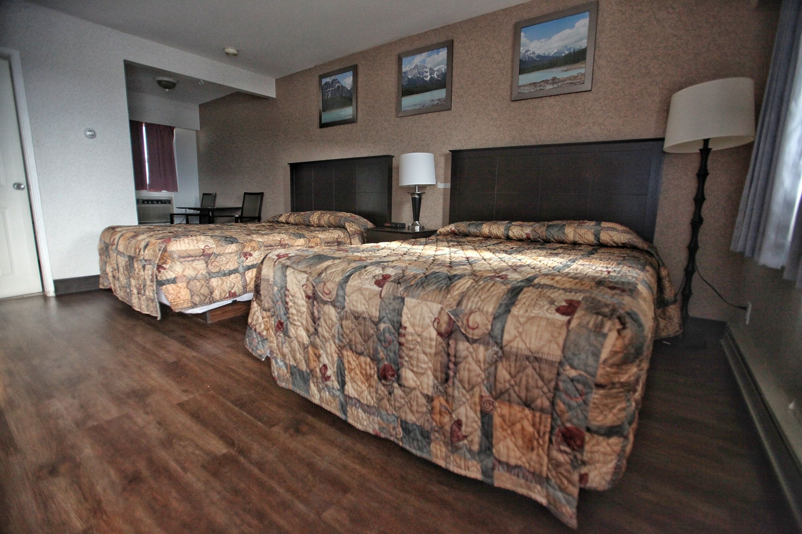 A hotel room with two beds, a desk, and a chair. There are three framed pictures on the wall.