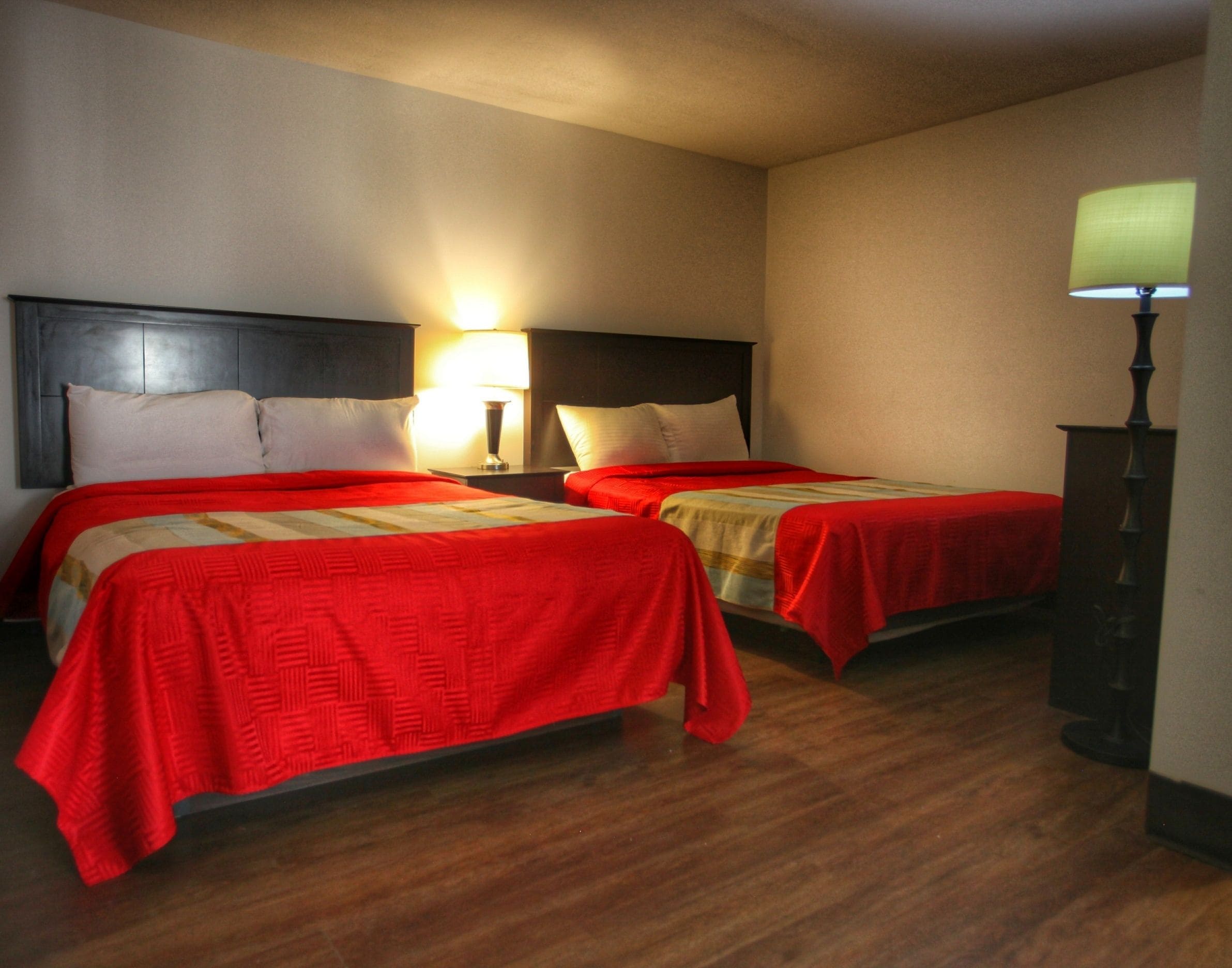 Habitación de hotel con dos camas, suelo de madera y una mesita de noche con lámpara.