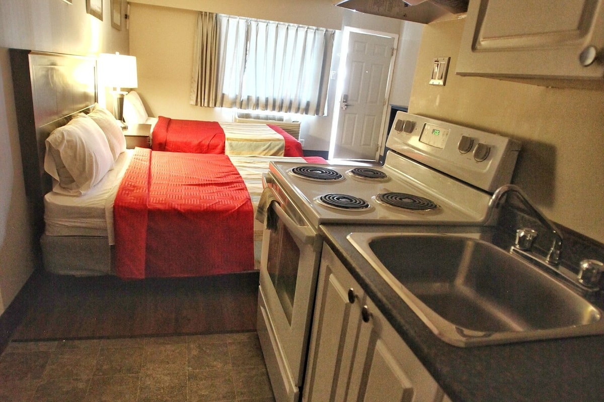 Eine kleine Hotelküche mit Herd, Spüle und einem Bett mit roter Decke.