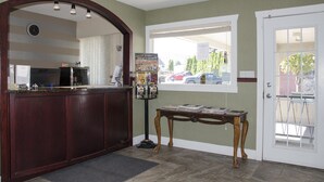 A reception area with a wooden reception desk, a clock, a window with a view of parked cars, and a bulletin board with various notices.