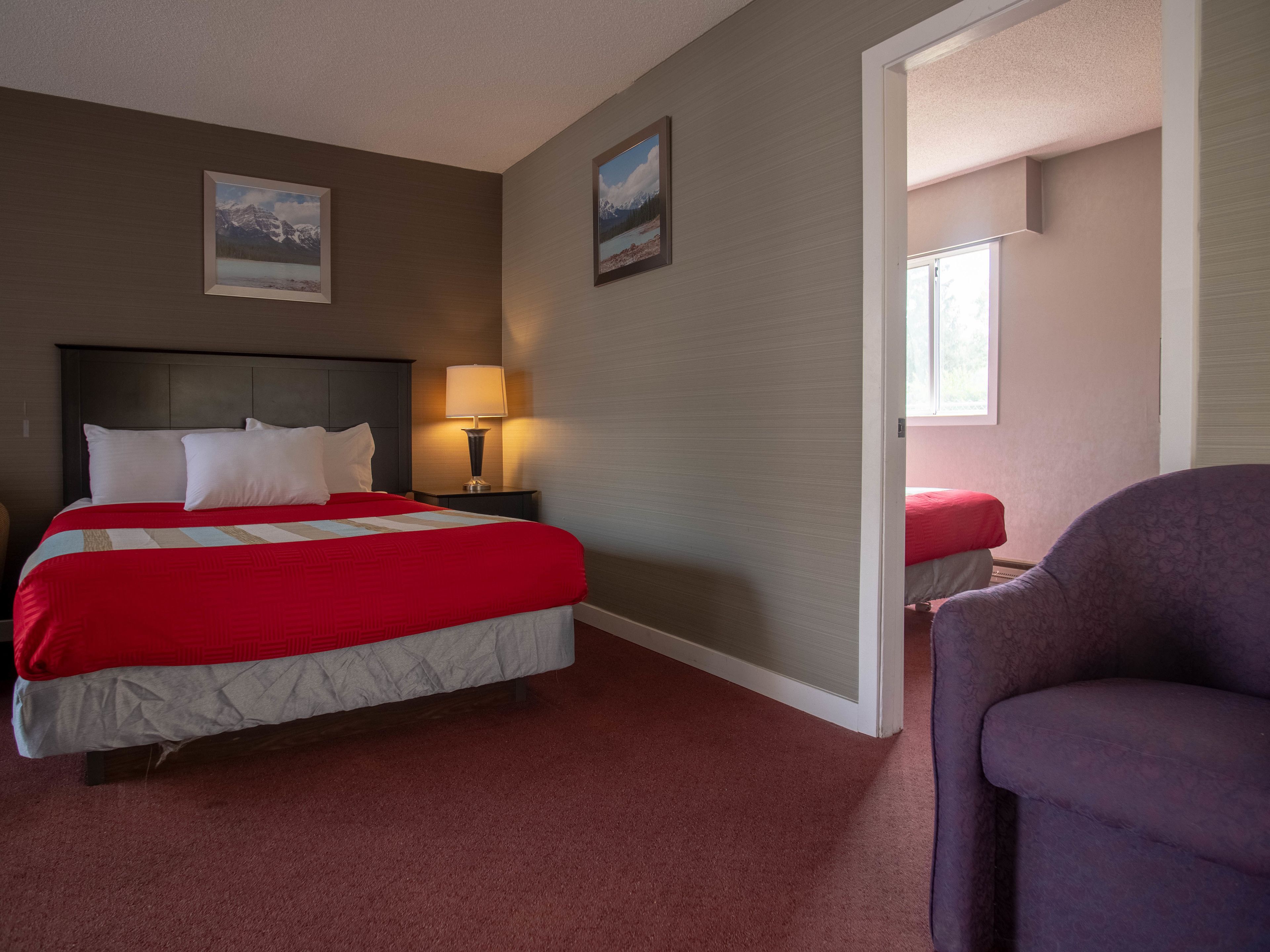 Une chambre d’hôtel avec un lit, une table de chevet, une lampe, une chaise et deux tableaux encadrés au mur.
