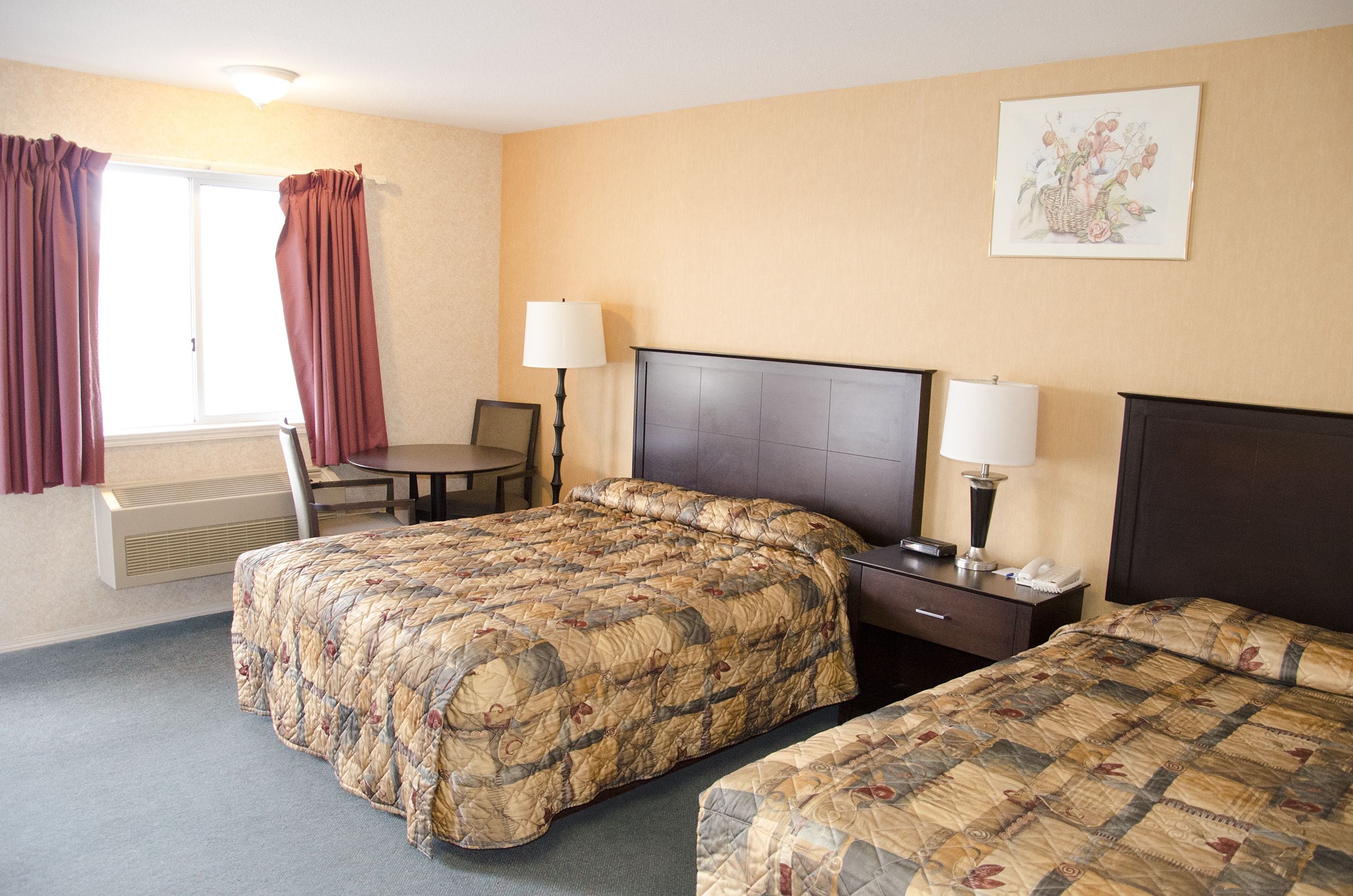 A hotel room with a large bed, a smaller bed, a desk with a chair, two bedside lamps, and a window with curtains.