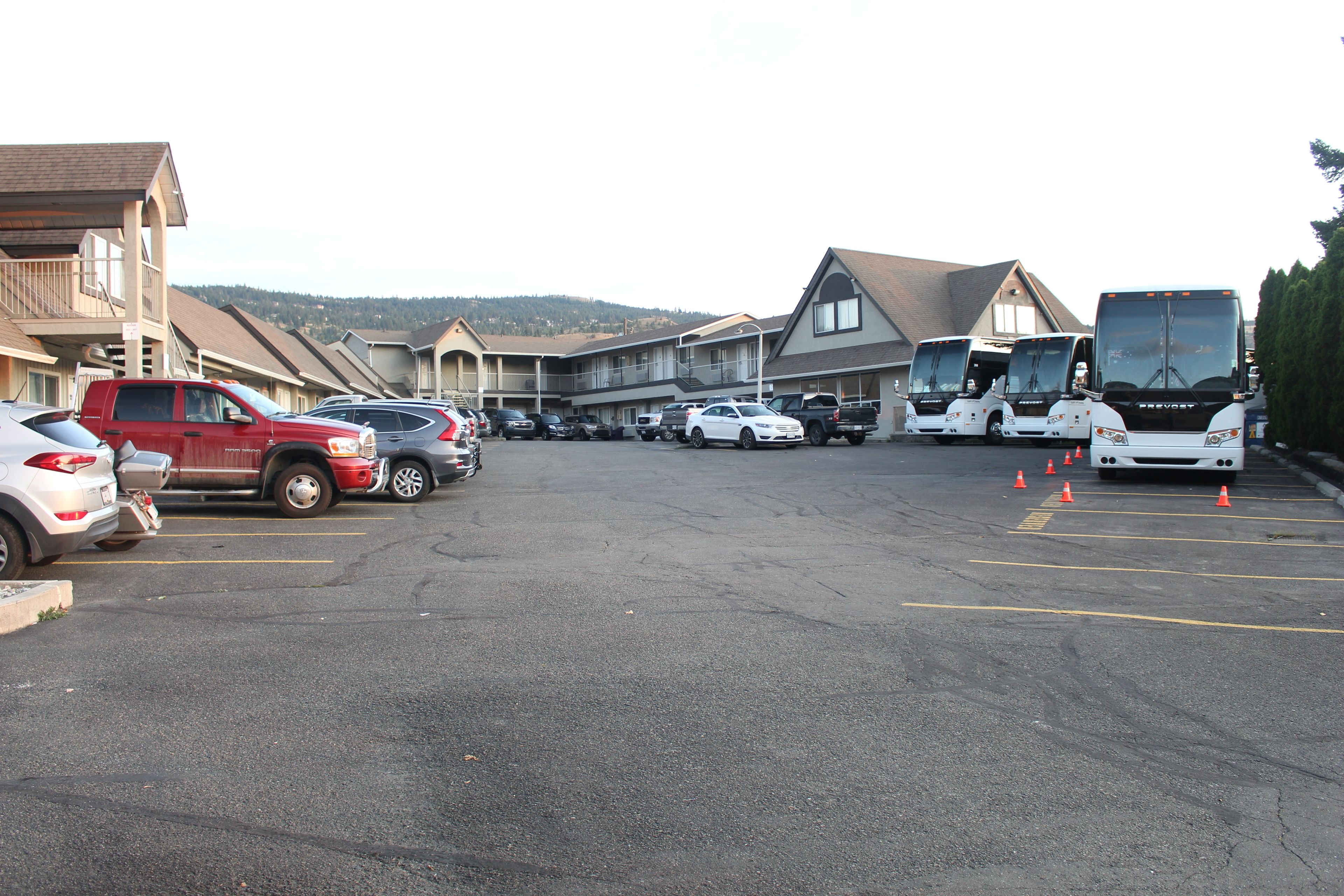 A parking lot with several cars and buses, a building with a balcony, and a view of hills in the background.