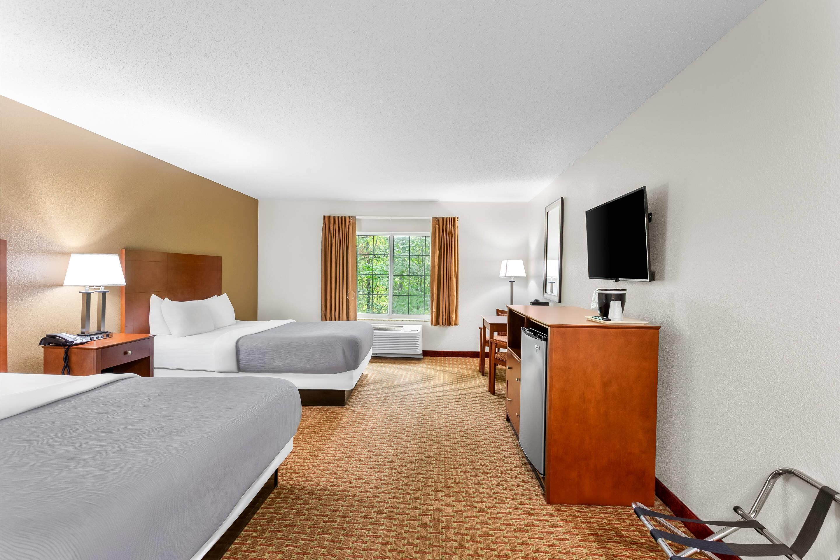 A hotel room with two beds, a desk, a TV, and a window with curtains.