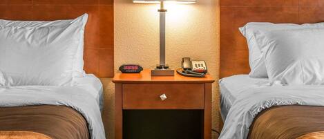 A hotel room with two beds, a nightstand with a lamp, a clock, and a telephone.