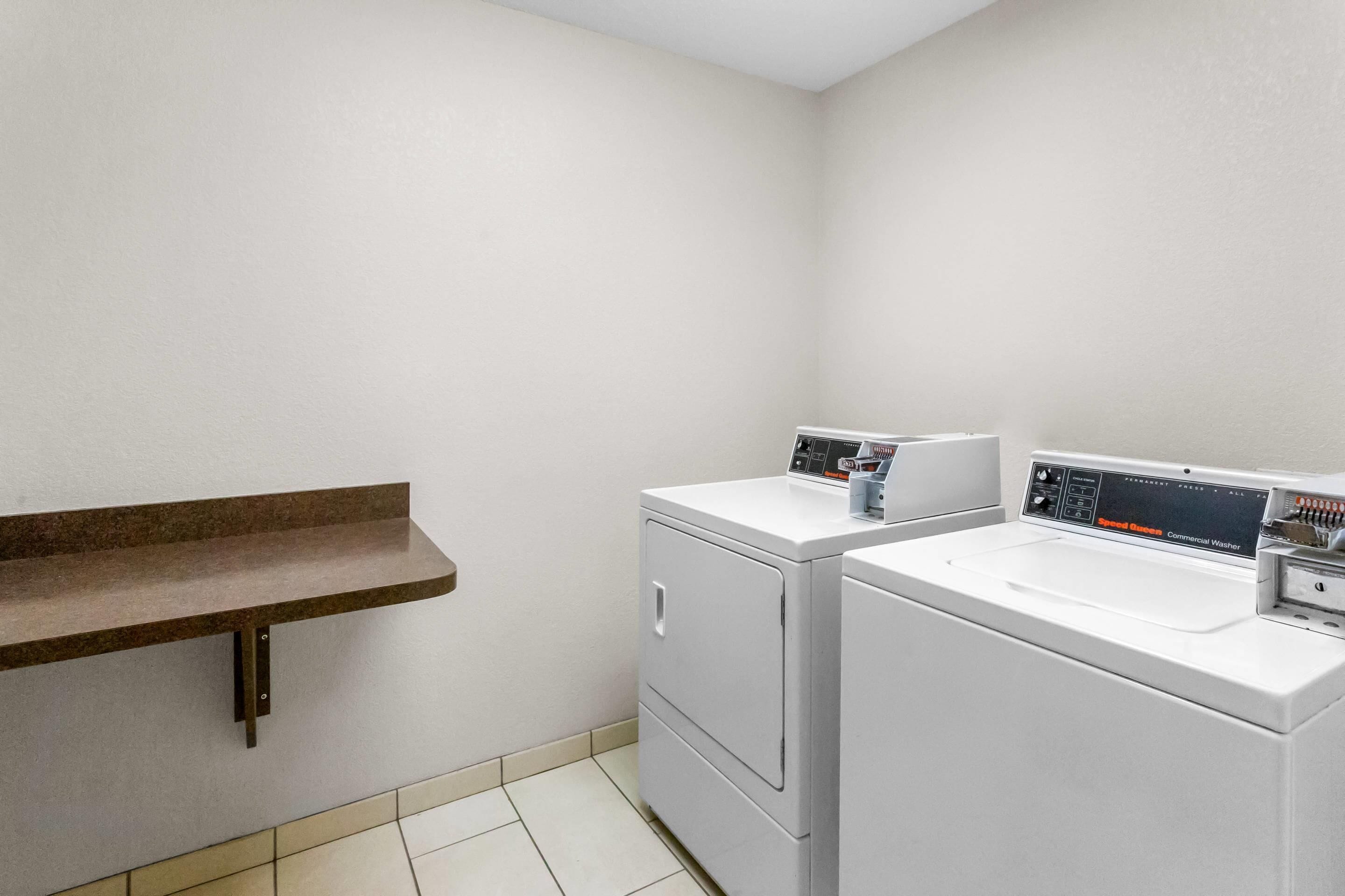 A laundry room with two white washing machines, a brown countertop, and a wall-mounted shelf.