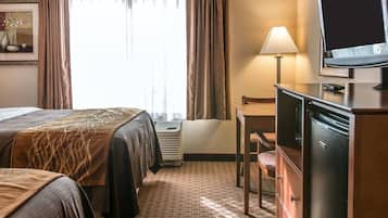 Una camera d'albergo con due letti, una scrivania con lampada, una televisione e un comò.