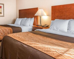 A hotel room with two beds, each with a brown headboard and a white lamp on a wooden nightstand.