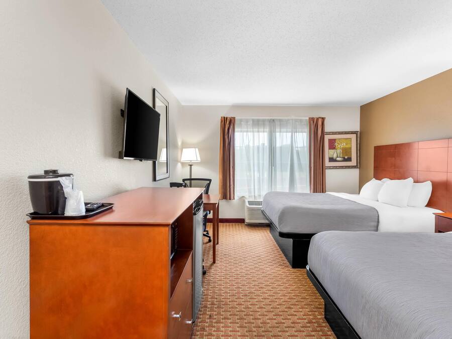 A hotel room with two beds, a desk with a coffee maker, a TV, and a window with curtains.