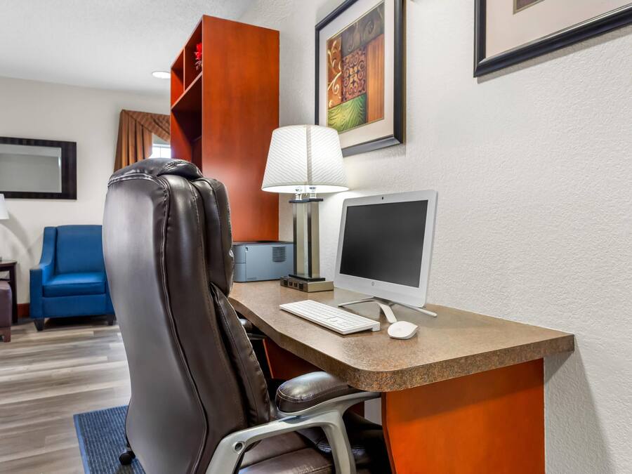 A hotel room with a desk, a computer, a chair, a lamp, a blue sofa, a small table with a lamp, and a framed picture on the wall.