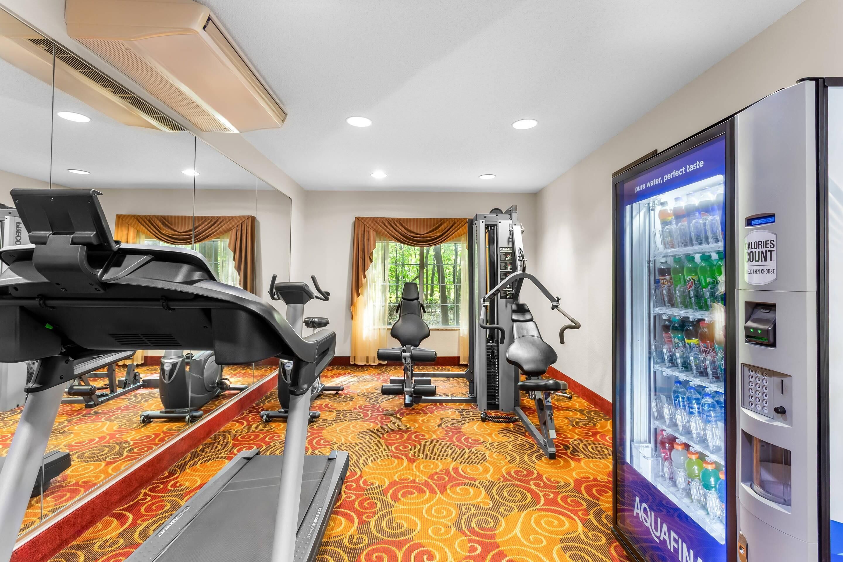 Ein Fitnessraum eines Hotels mit Trainingsgeräten, einem Wasserspender und gemustertem Teppichboden.