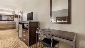 A hotel room with a desk, chair, television, and a large mirror. - Quality Inn Madisonville (Madisonville)