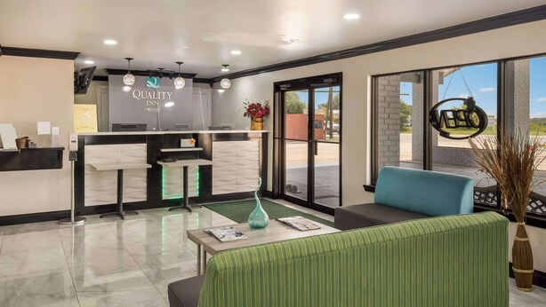 A hotel reception area with a reception desk, a waiting area with a sofa and a coffee table, and large windows offering a view of the outdoors. - Quality Inn Madisonville (Madisonville)