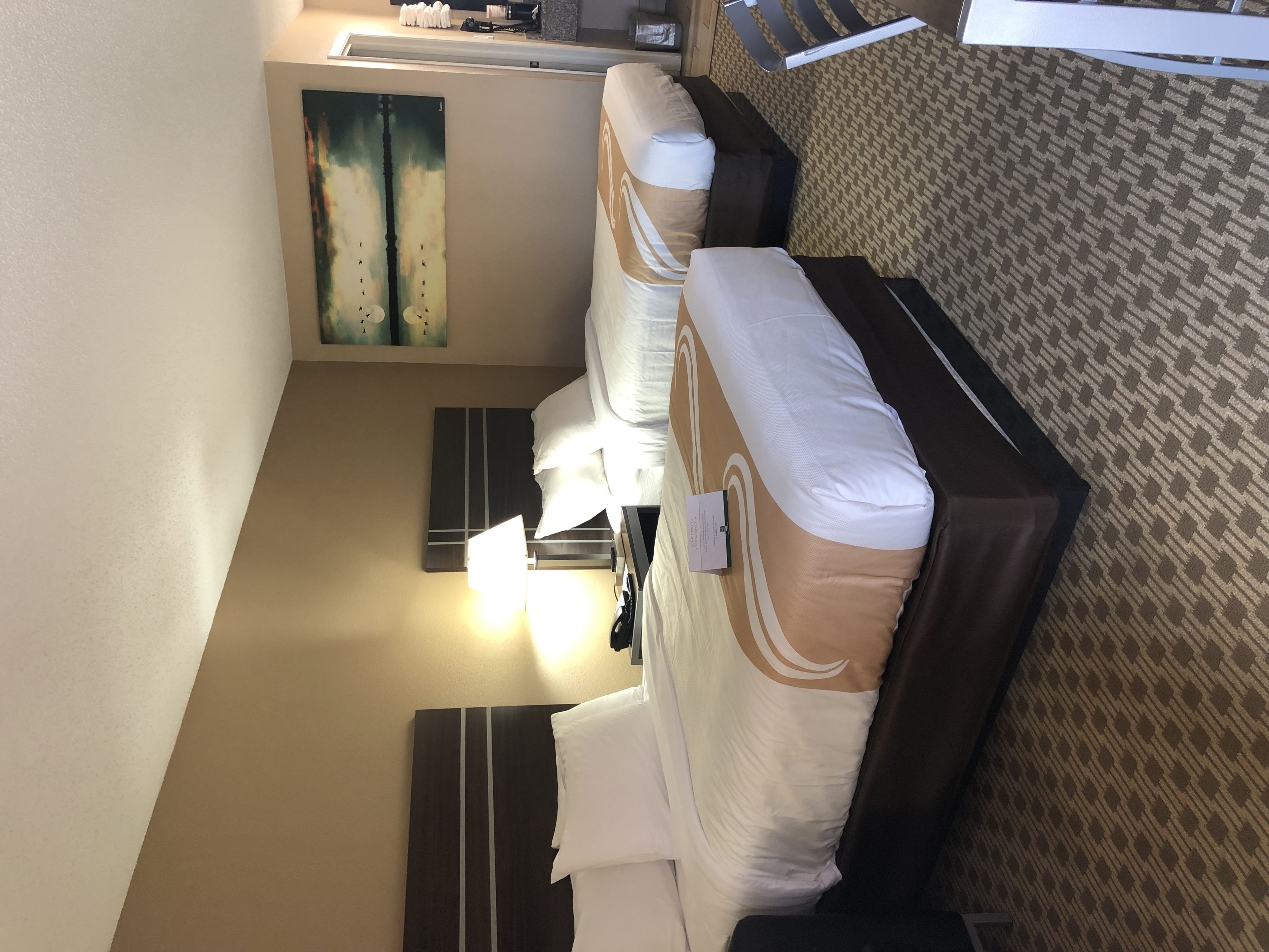 Una habitación de hotel con una cama, una mesita de noche, una lámpara y un cuadro en la pared.
