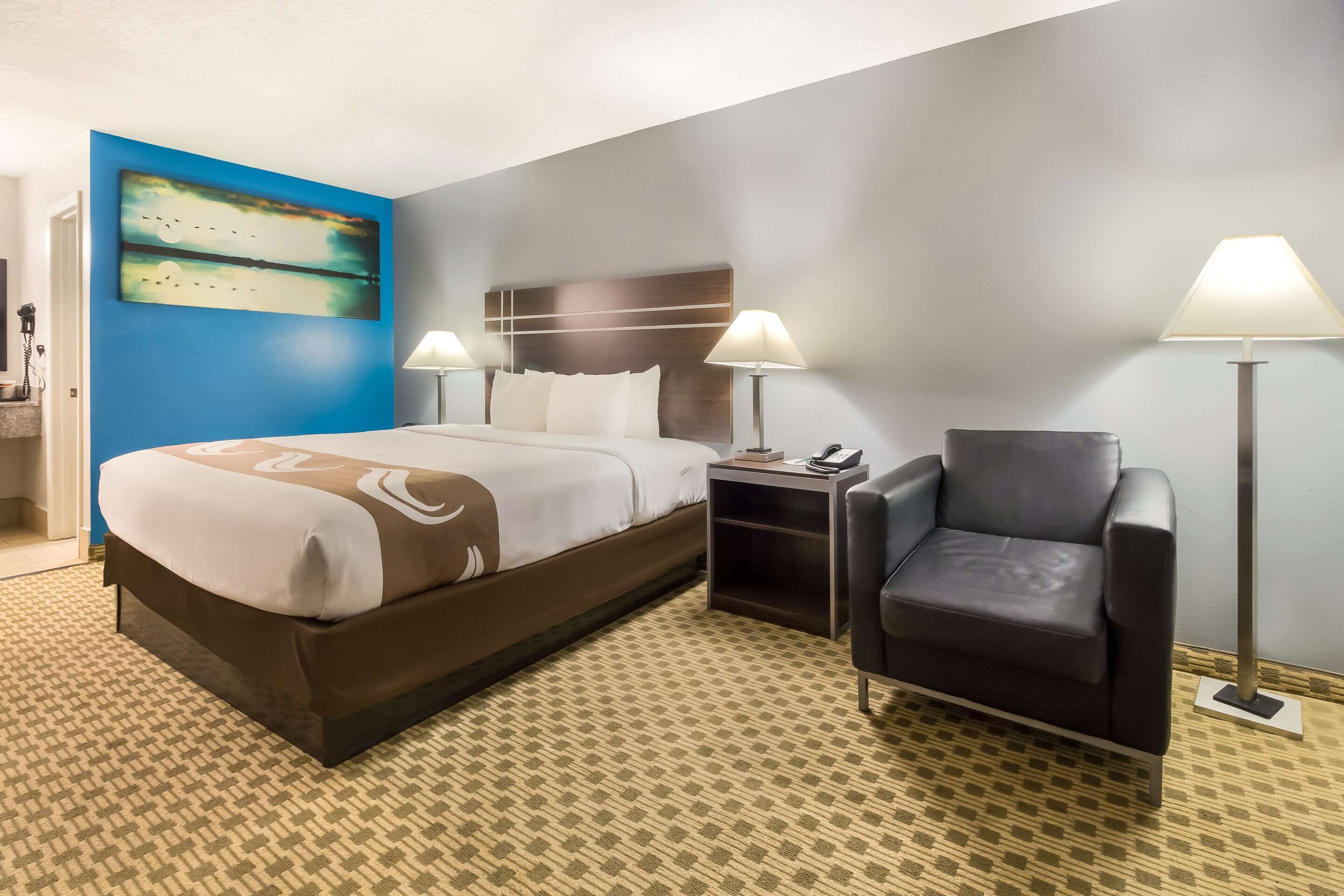 Ein Hotelzimmer mit einem großen Bett, zwei Nachttischlampen, einem Sessel und einem Nachttisch.