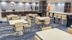 A hotel dining area with multiple tables and chairs, a counter with a coffee machine, and a wall with framed pictures. - Wingate by Wyndham Panama City Area Lynn Haven (Lynn Haven)