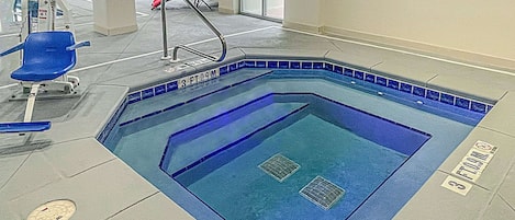 An indoor swimming pool with a blue tiled edge, a diving board, and a lifeguard chair.