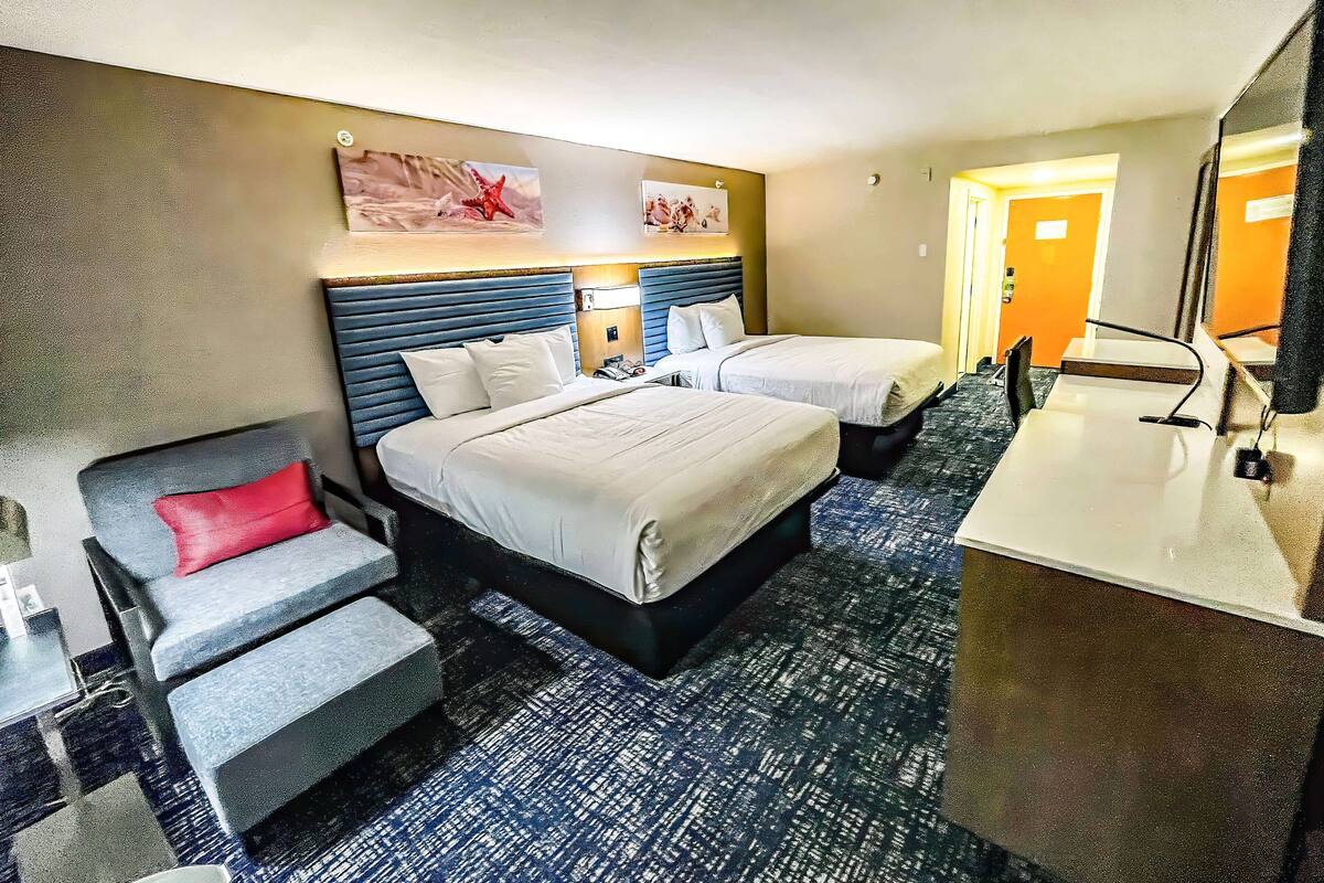 Une chambre d’hôtel avec deux lits, un bureau, une chaise et un miroir.