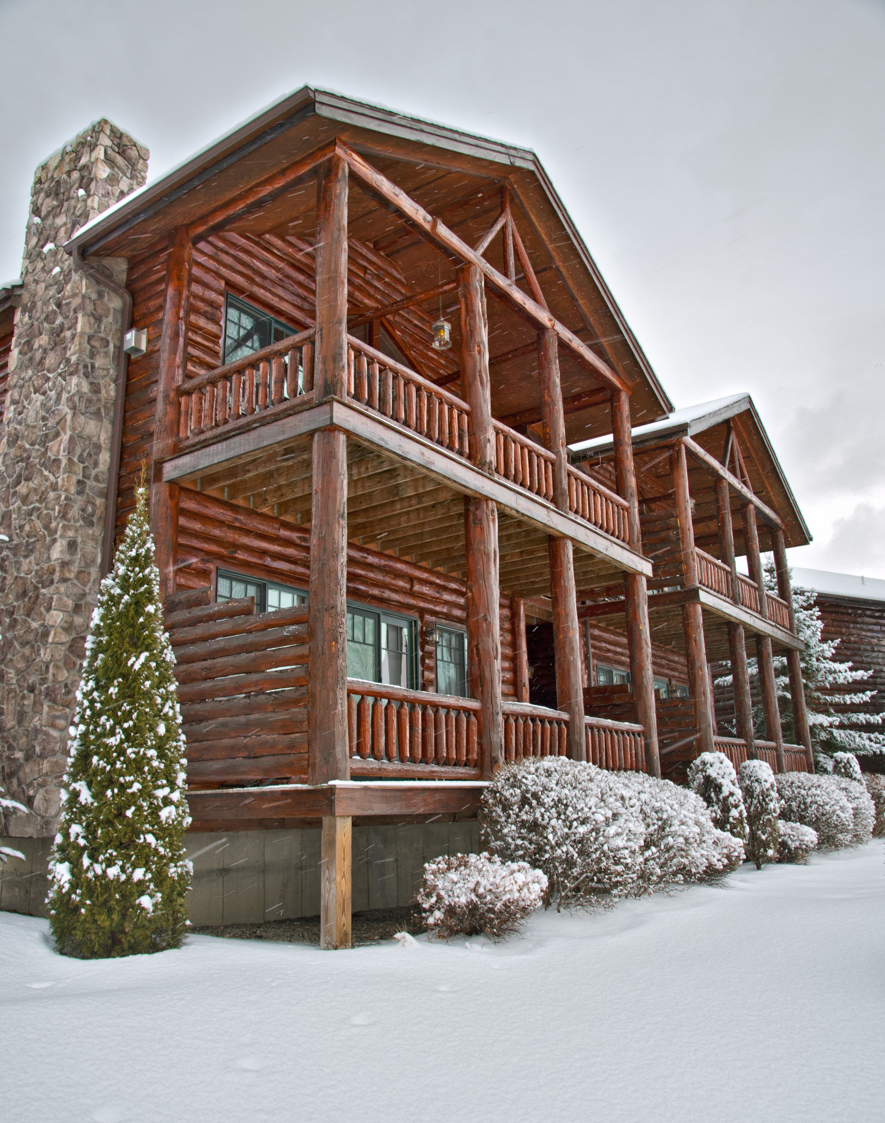 A multi-story log cabin with a stone chimney, balconies, and snow-covered surroundings.