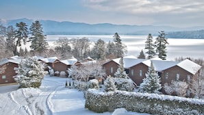 A snow-covered lodge with cabins, a clear view of a lake, and mountains in the background.