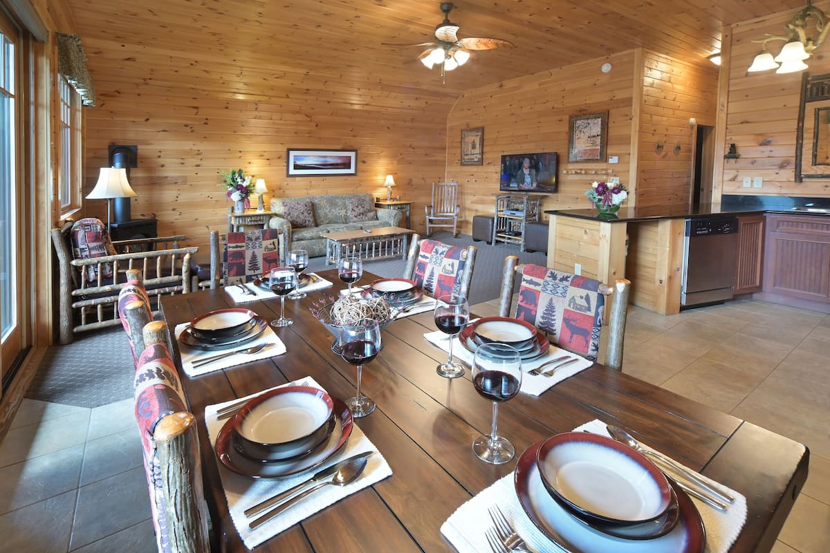 A wooden interior with a dining table set for a meal, a sofa, and a fireplace.
