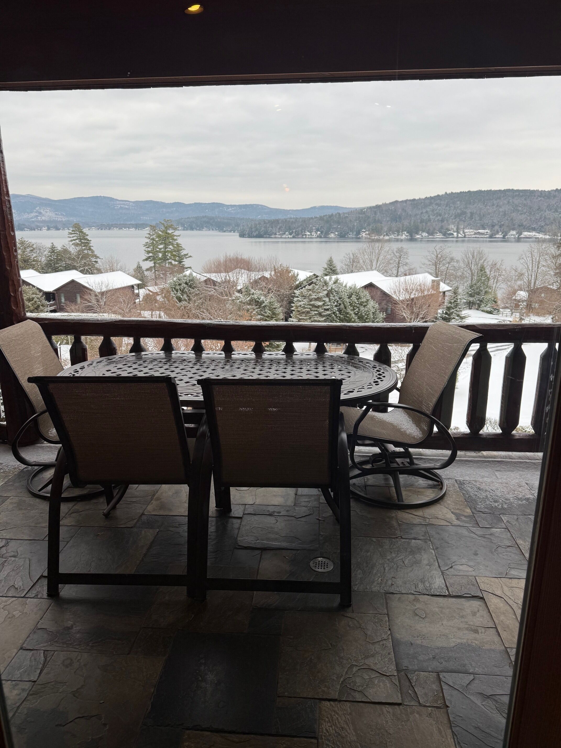 A balcony with a table and chairs, overlooking a lake and mountains.