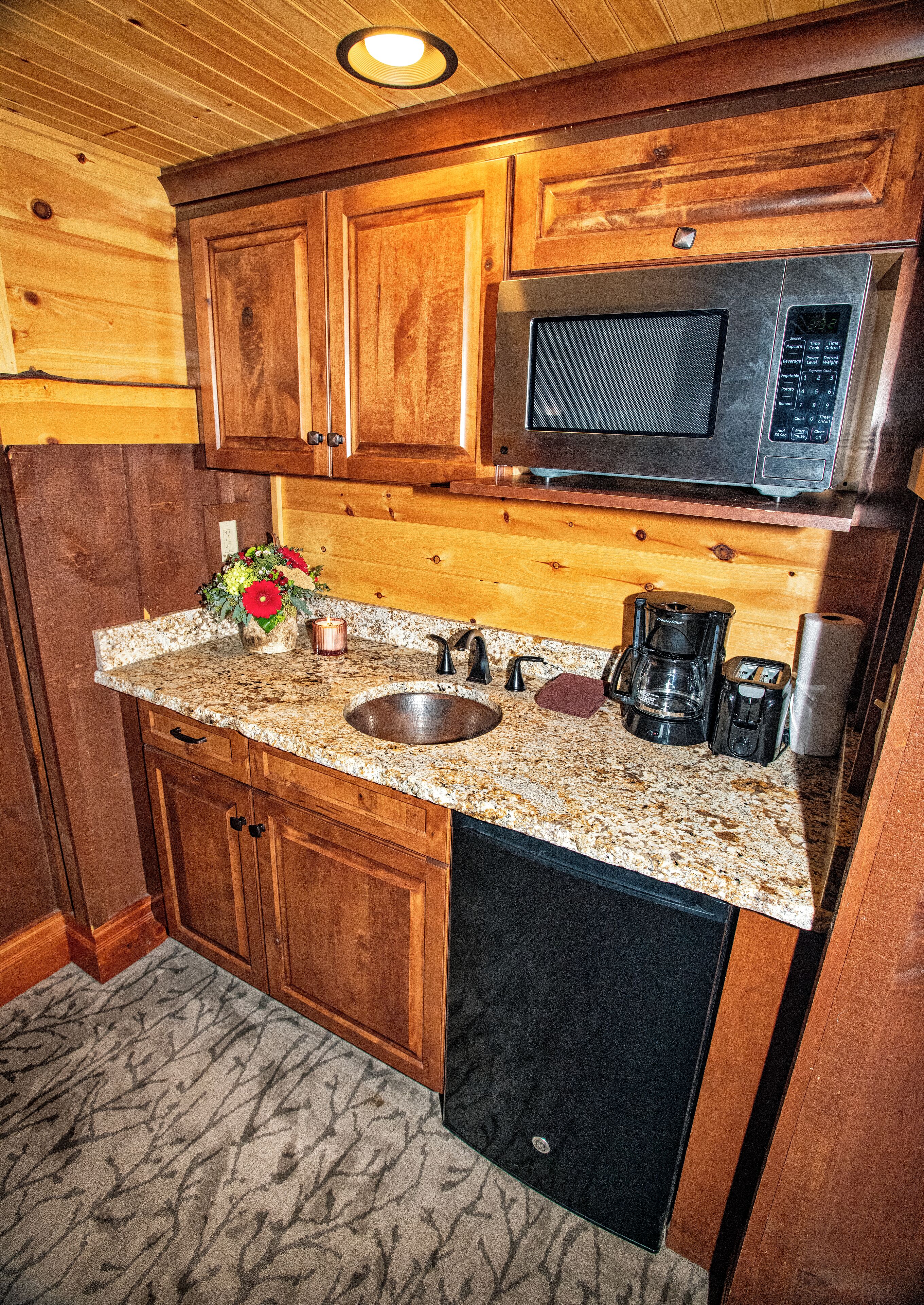 A kitchen with wooden cabinets, a granite countertop, a stainless steel microwave, a coffee maker, and a dishwasher.