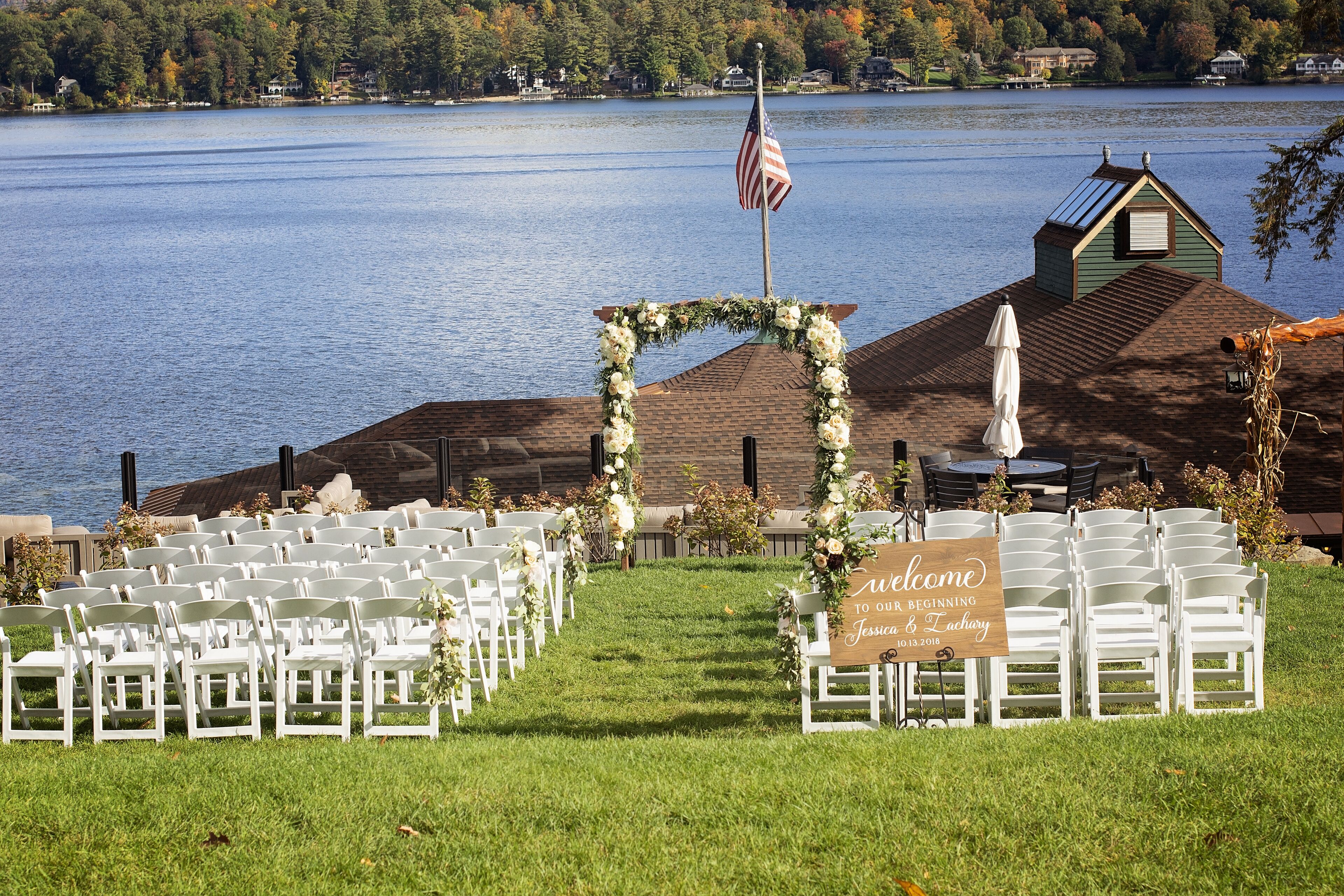 A lakeside wedding venue with rows of white chairs and a welcome sign.