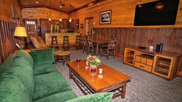 Un acogedor interior de cabaña de madera con un sofá verde, una mesa de comedor de madera y un televisor montado en la pared.