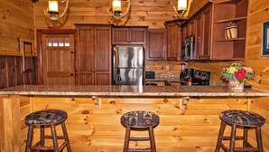 A wooden cabin interior with a kitchen featuring a stainless steel refrigerator, wooden cabinets, and a bar area with stools.