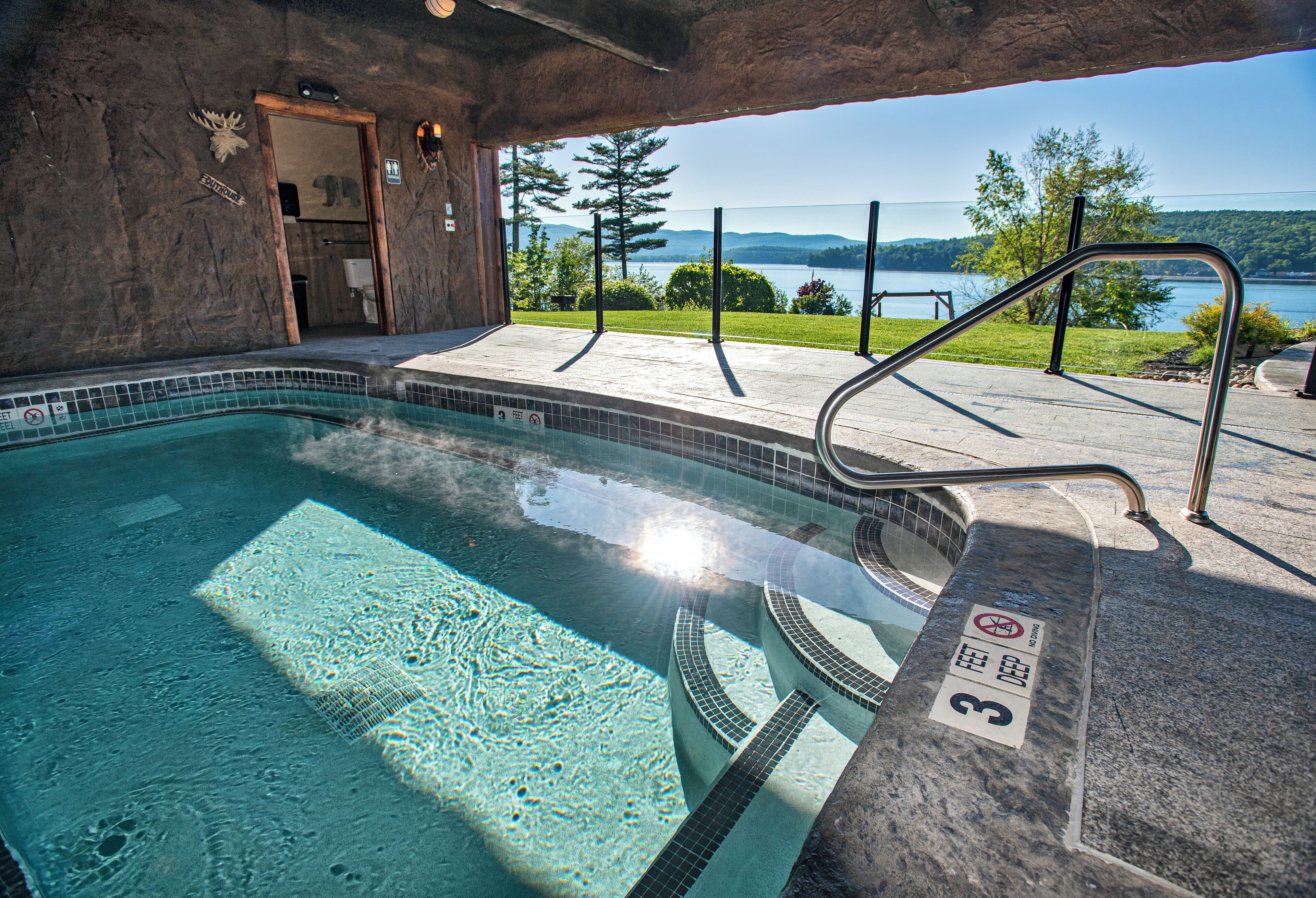A swimming pool with a view of a lake and mountains, a wooden door, and a 'No Diving' sign.