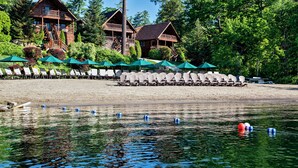 A lakeside lodge with a wooden exterior, a deck, and a row of beach chairs under umbrellas.