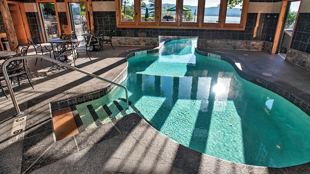 An indoor swimming pool with clear water, surrounded by stone walls and wooden windows.